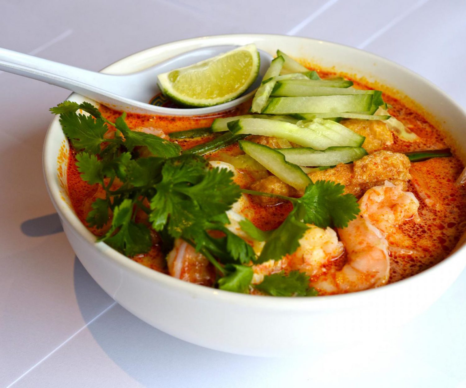 Soup bowl filled with prawns, coriander, cucumber slices and a slice of lime on top of the spoon