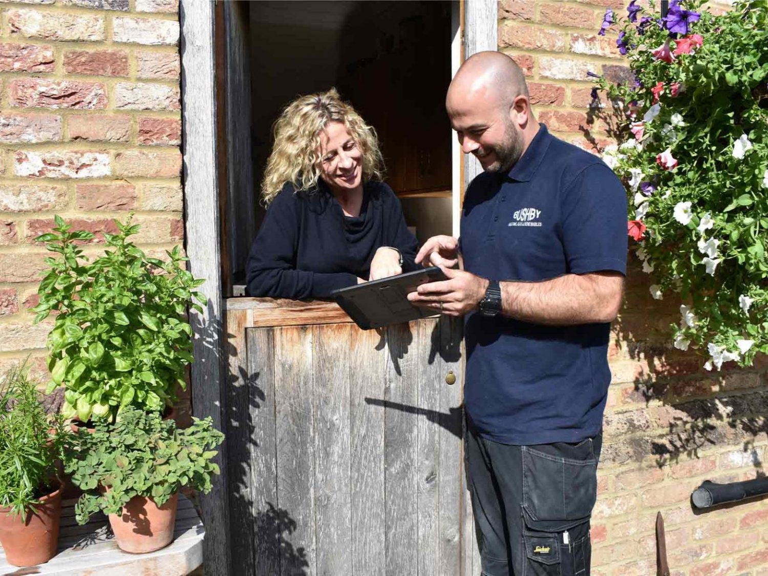 A plumber showing something on his notepad to a woman leaning on her dutch door